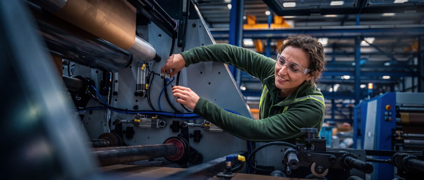 Vrouw met veiligheidsbril werkt aan industriële machine in een fabriek
