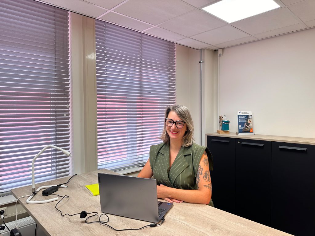 Vrouw met bril werkt aan een bureau met laptop in een modern kantoor